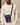 man wearing beige crewneck and a navy crossbody sling bag with black strap and front pocket with red logo