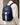 person wearing a navy backpack with a white circular logo and a pale stripe, front zip pocket and mesh side pocket