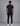 back view of a man wearing a black short sleeve tee with black jeans and white sneakers against a grey studio backdrop