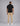 back view of a man wearing a black short sleeve knit polo and beige chinos with white sneakers